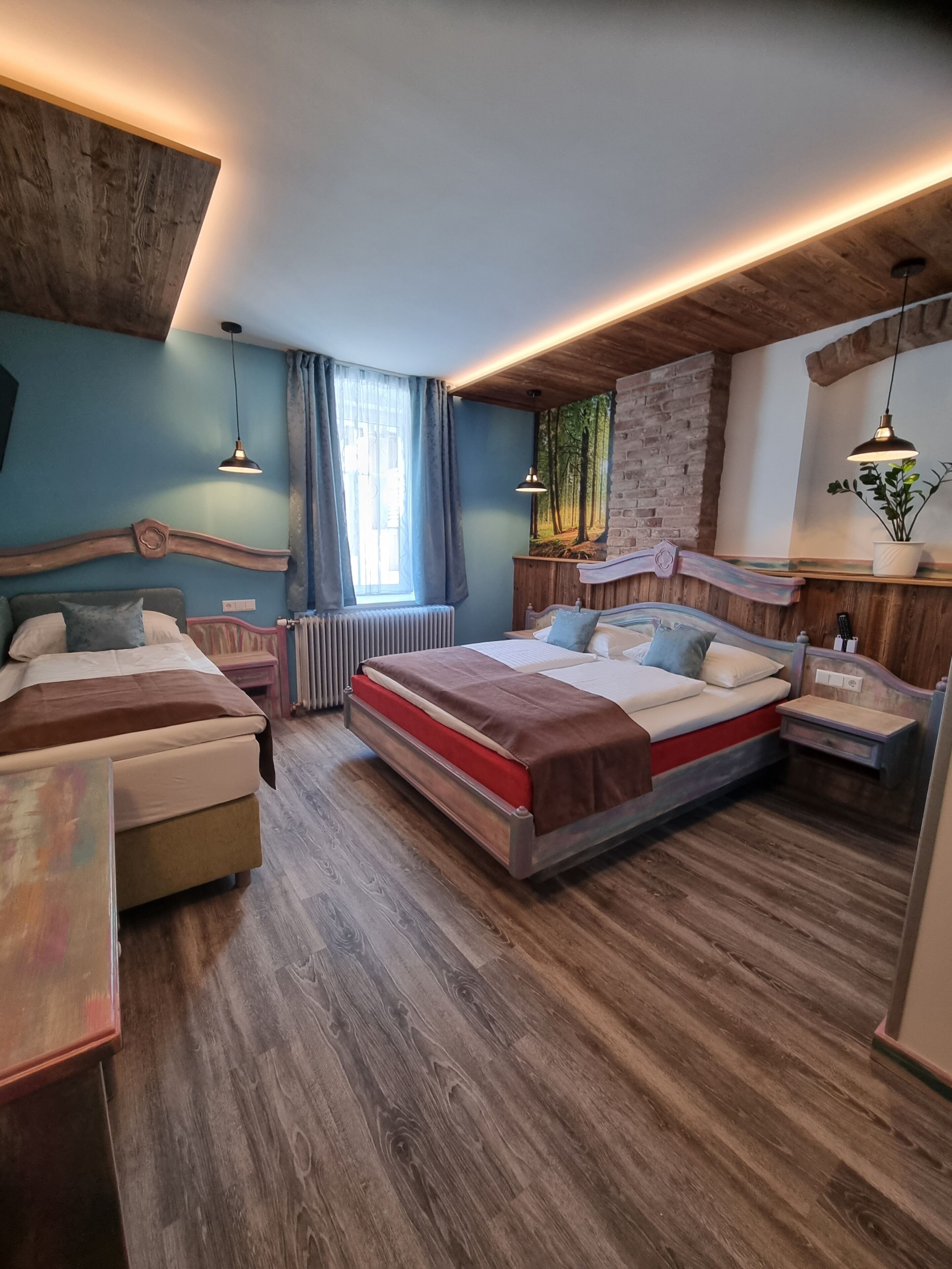 A modern bedroom with two beds, a wooden floor, a brick wall, and a large window.