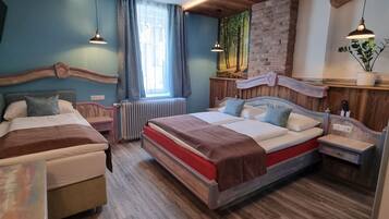 A modern bedroom with two beds, a wooden floor, a brick wall, and a large window.