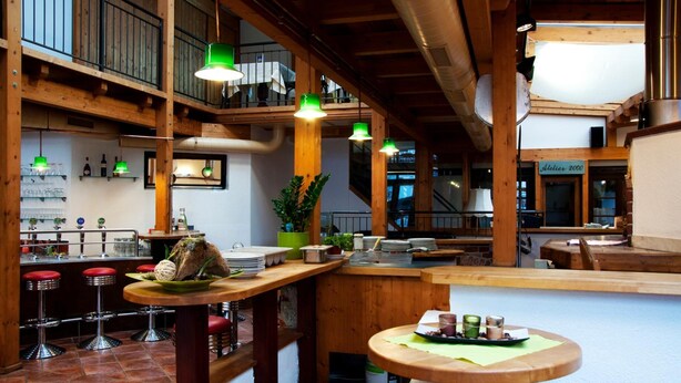 A restaurant with wooden beams, green pendant lights, and a bar area with stools. - Hotel Torwirt (Wolfsberg)