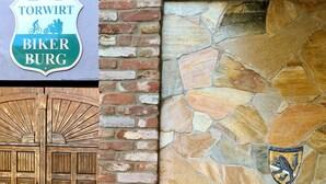 A brick wall with a stone mosaic and a wooden door with a crest emblem. - Hotel Torwirt (Wolfsberg)