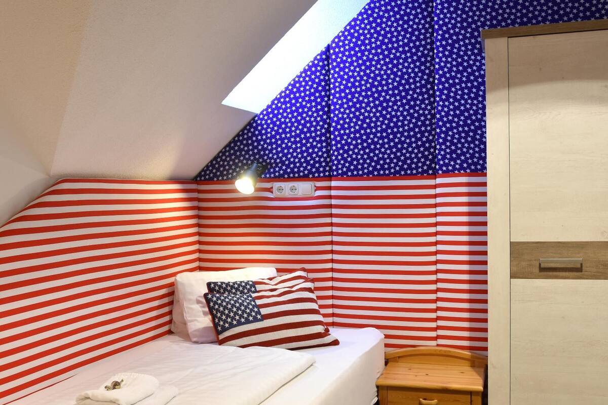 A small, cozy room with a bed, a nightstand, and a wooden wardrobe.