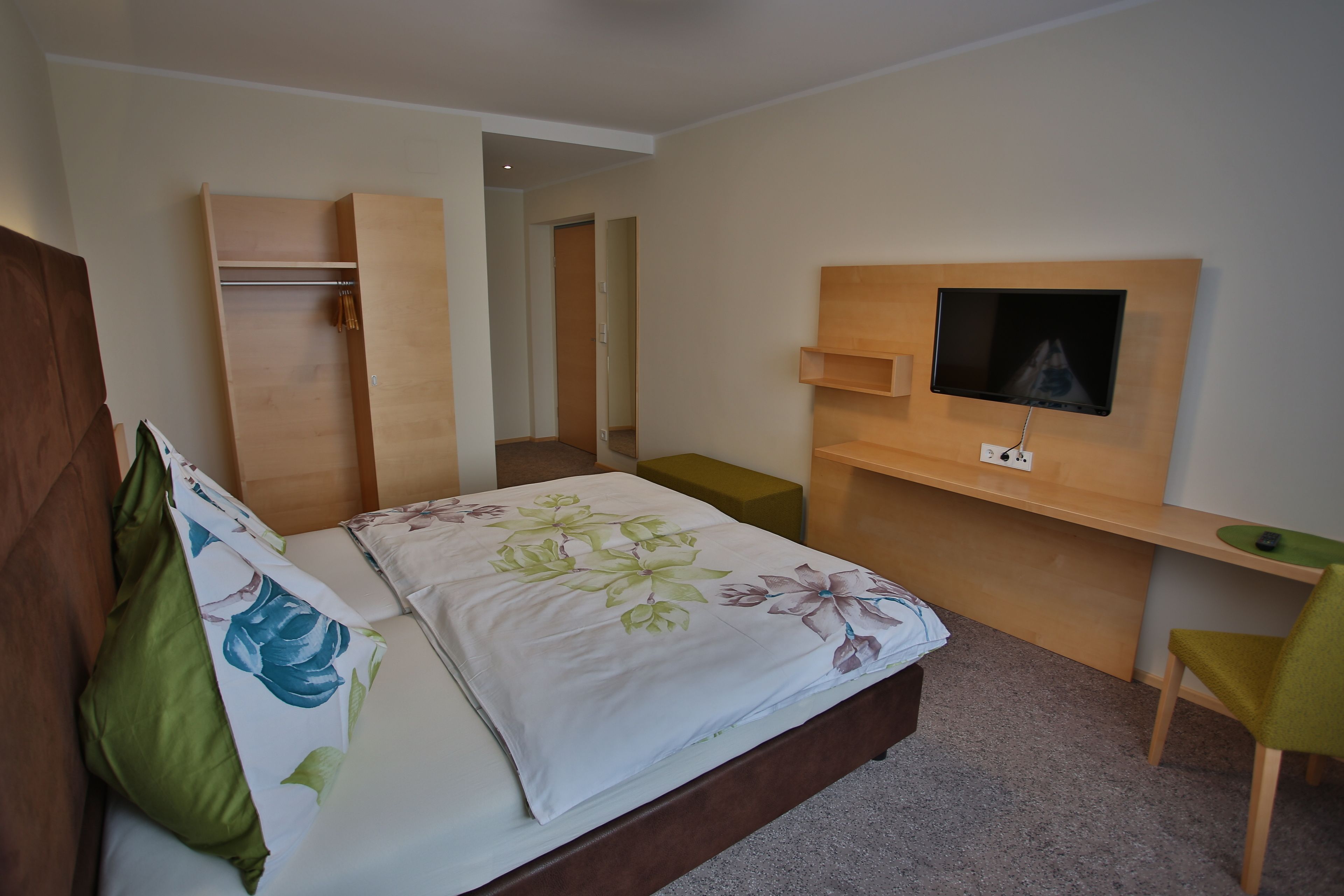 Un dormitorio con una cama, un televisor montado en una pared de madera, un escritorio y una silla.