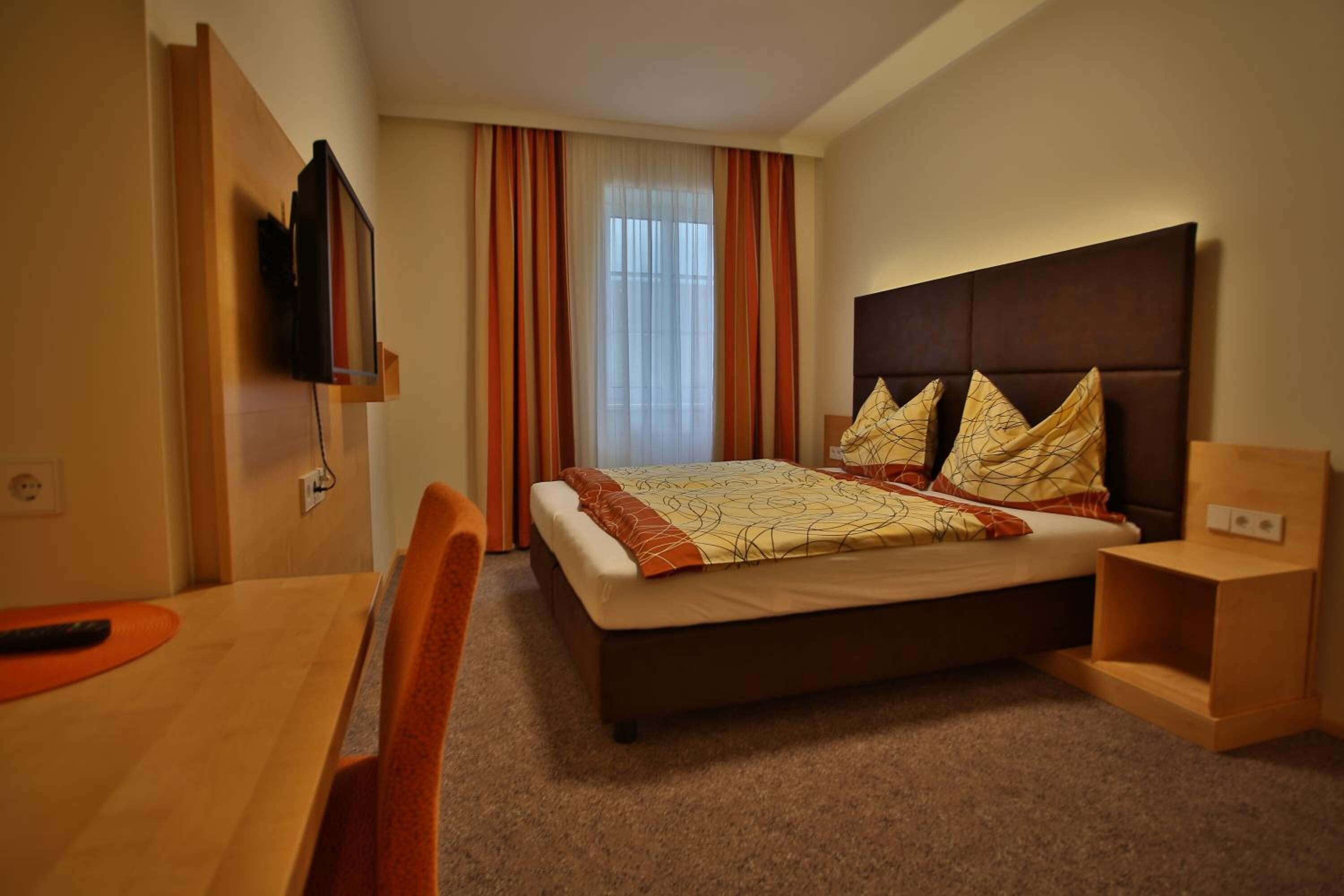 A hotel room with a bed, a TV mounted on the wall, a desk, and a chair.