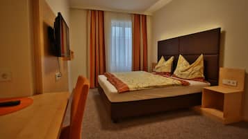 A hotel room with a bed, a TV mounted on the wall, a desk, and a chair.
