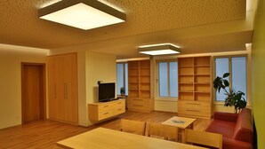 A modern living room with a wooden floor, a red sofa, a wooden dining table, and built-in shelves. - Gasthof Alpenblick (Ardagger Markt)