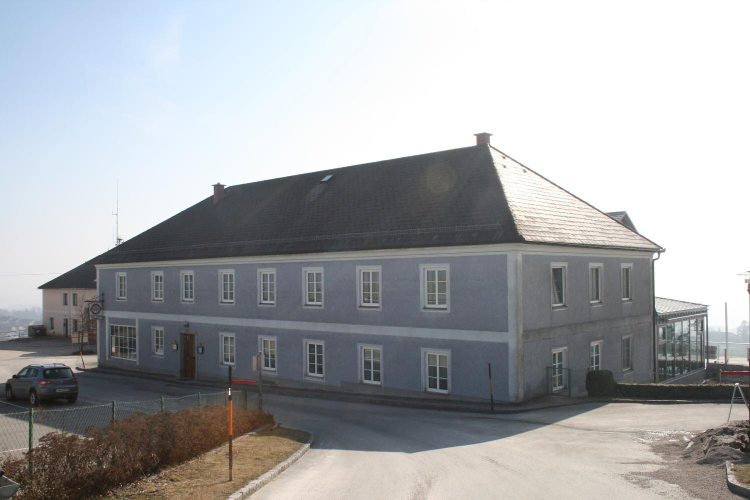 A two-story building with a grey facade, multiple windows, and a sloped roof.