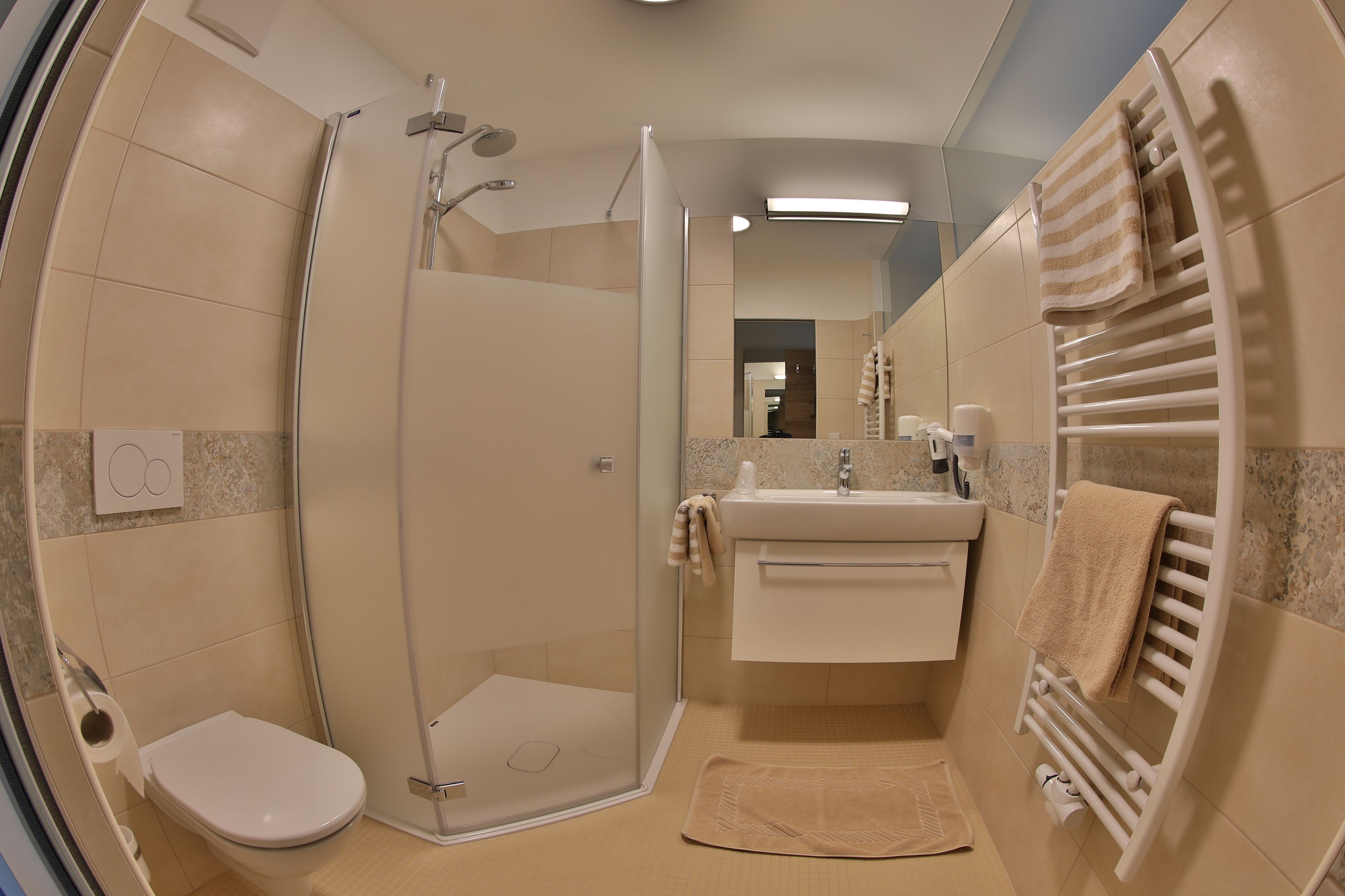 Un baño moderno con ducha envuelta en vidrio, un inodoro, un lavabo con toallero y un espejo.
