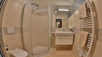 Un baño moderno con ducha envuelta en vidrio, un inodoro, un lavabo con toallero y un espejo.