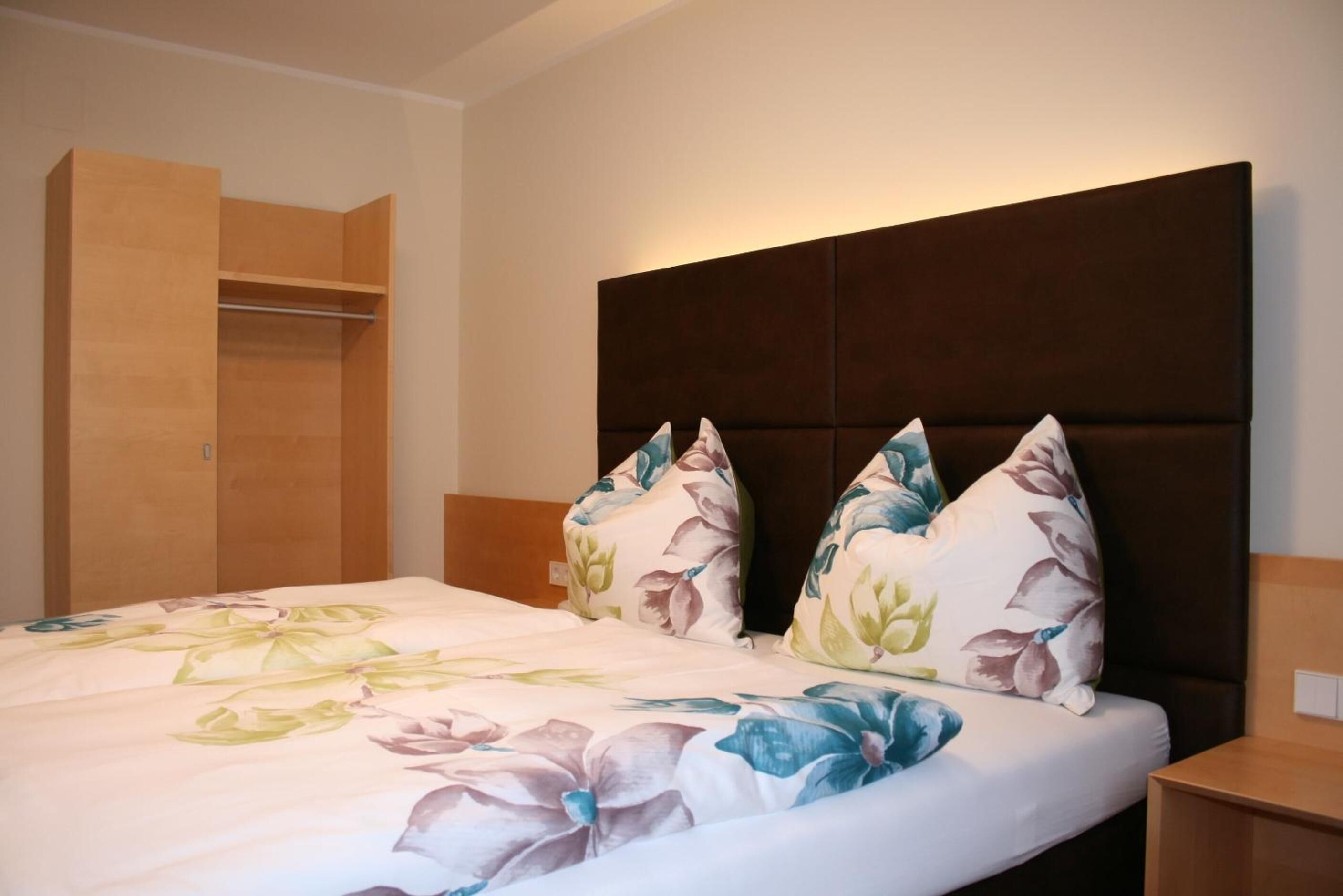 Una habitación de hotel con una cama, un armario de madera y una mesita de noche.