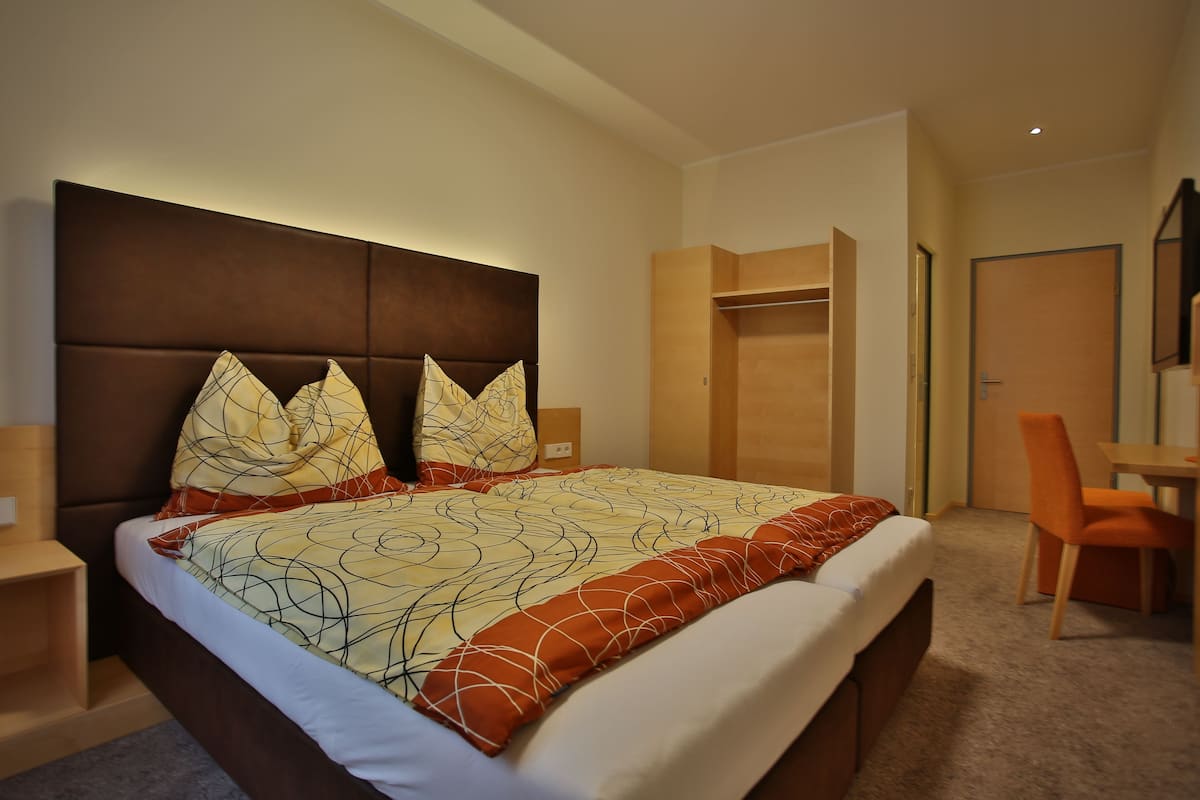 A modern hotel room with a large bed, a desk, and a wardrobe.
