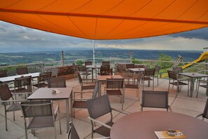 An outdoor patio with tables and chairs, a yellow slide, and a scenic view of the countryside. - Gasthof Alpenblick (Ardagger Markt)