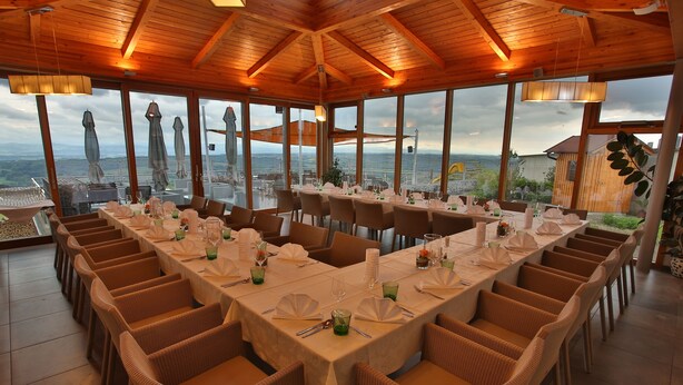 A restaurant with large windows offering a scenic view, wooden ceiling, and wicker chairs. - Gasthof Alpenblick (Ardagger Markt)