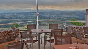 A terrace with a table and chairs, overlooking a scenic landscape with mountains and fields. - Gasthof Alpenblick (Ardagger Markt)