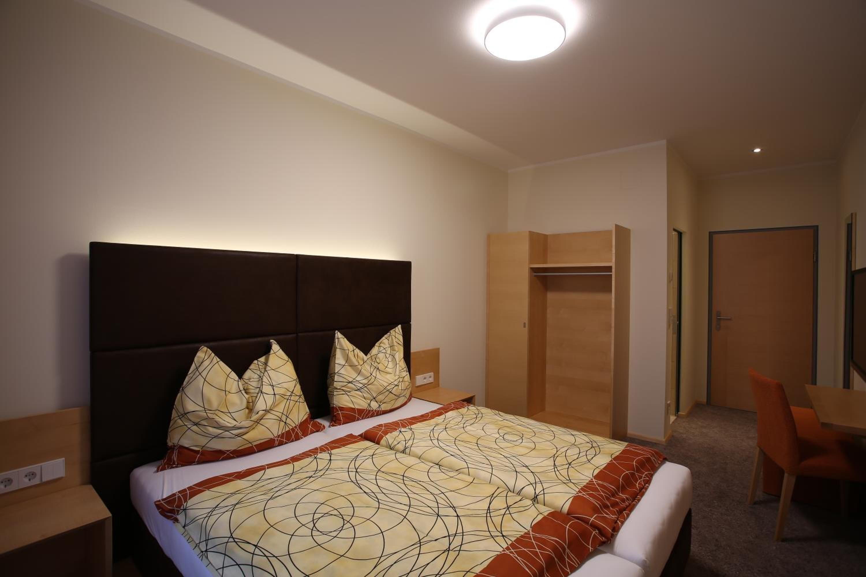Habitación de hotel con una cama grande, una mesita de noche, una silla, un armario y un escritorio.