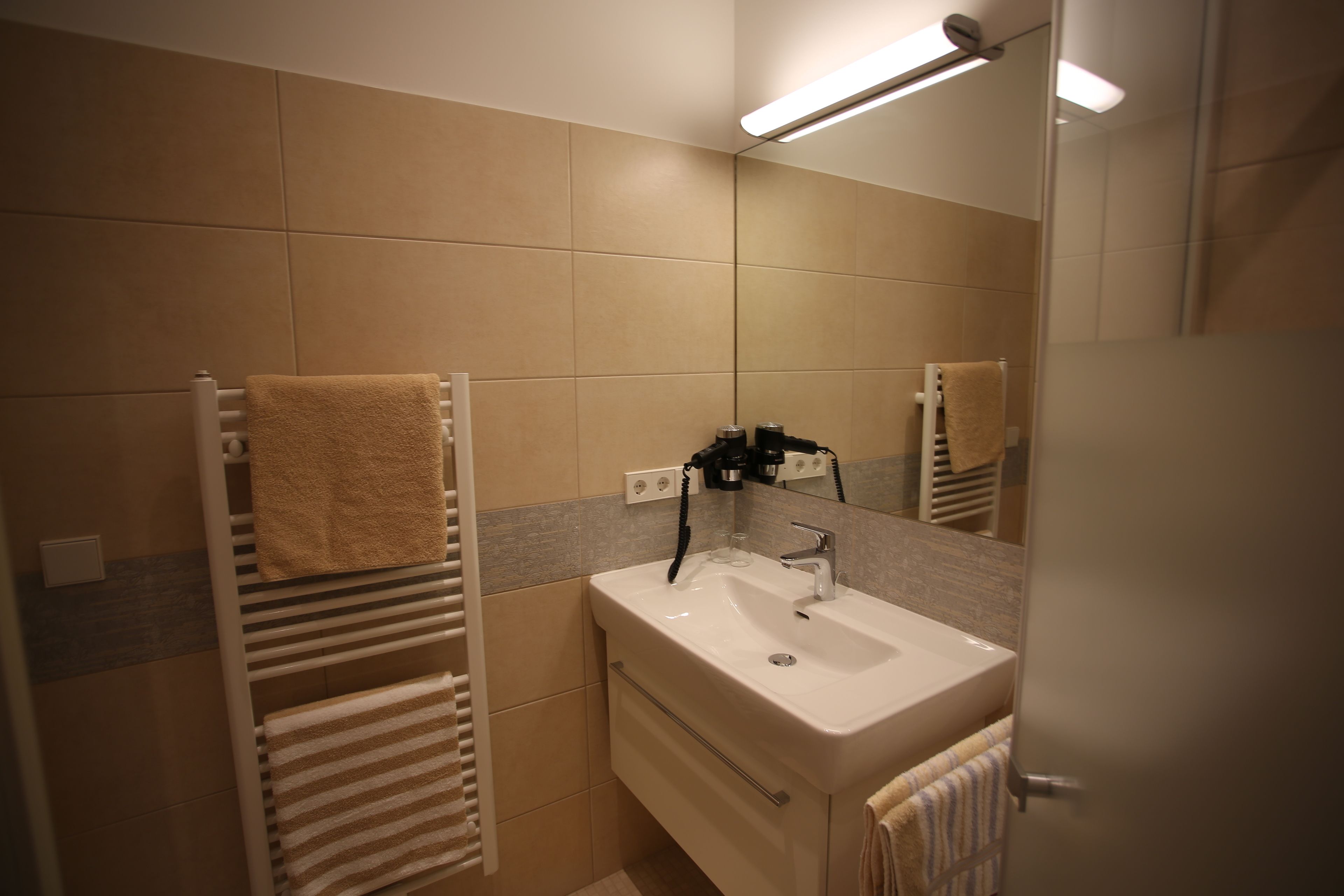 A bathroom with a white sink, a mirror, and two towel racks with towels.