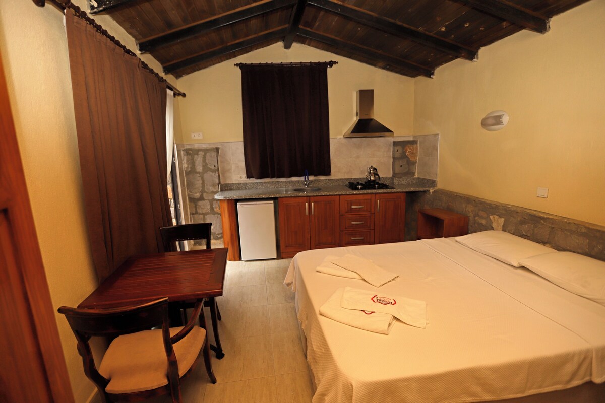 Una habitación con cama, un escritorio pequeño, una silla, una kitchenette y una ventana con cortinas.