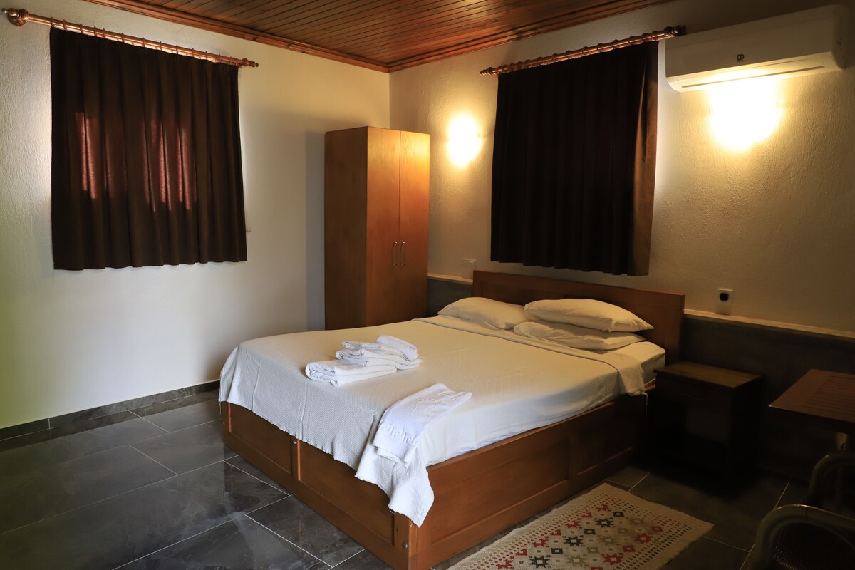 Un dormitorio con cama de madera, ropa de cama blanca, un armario, una mesita de noche y un aire acondicionado de pared.