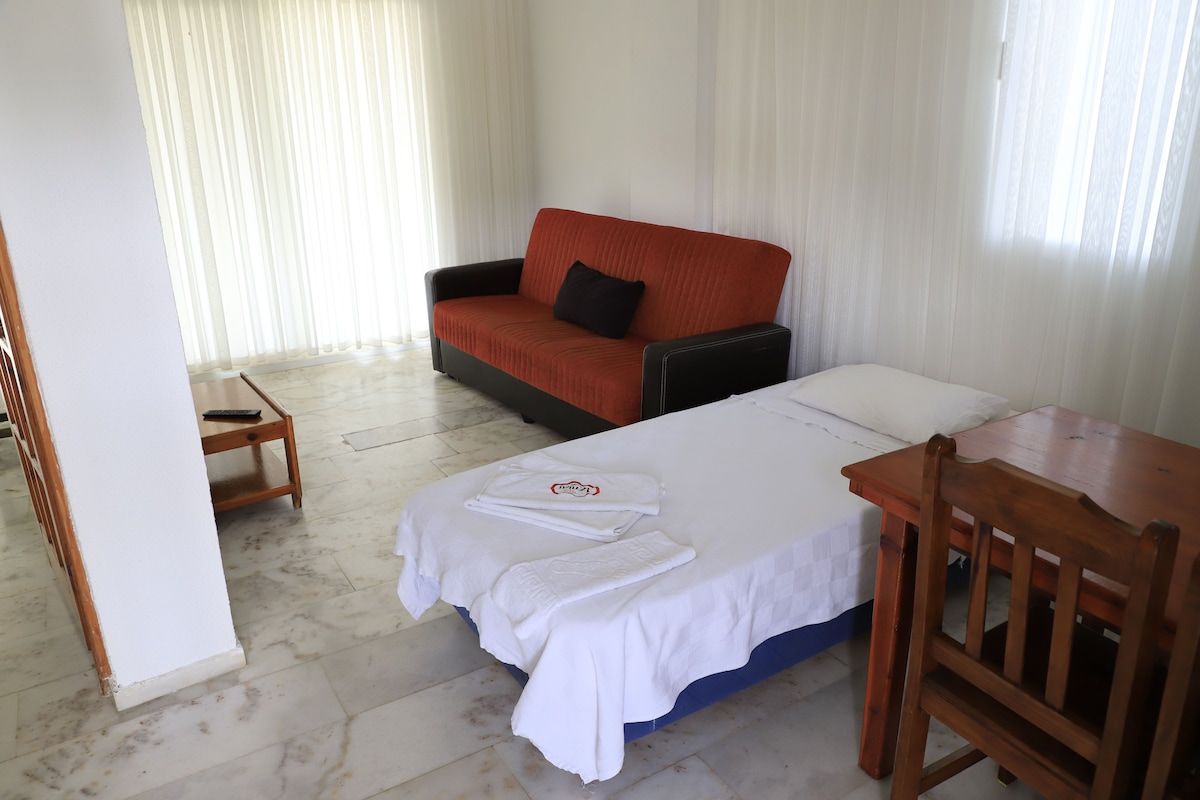 Una habitación de hotel con una cama, un sofá rojo, una silla de madera y una mesita.