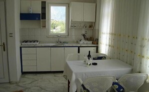 Uma cozinha compacta com armários brancos, fogão a gás e uma janela. Há uma área de refeições com mesa e cadeiras.