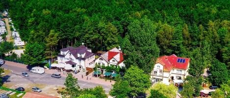 A hotel with a red roof, surrounded by dense forest and a clear view of the sea.