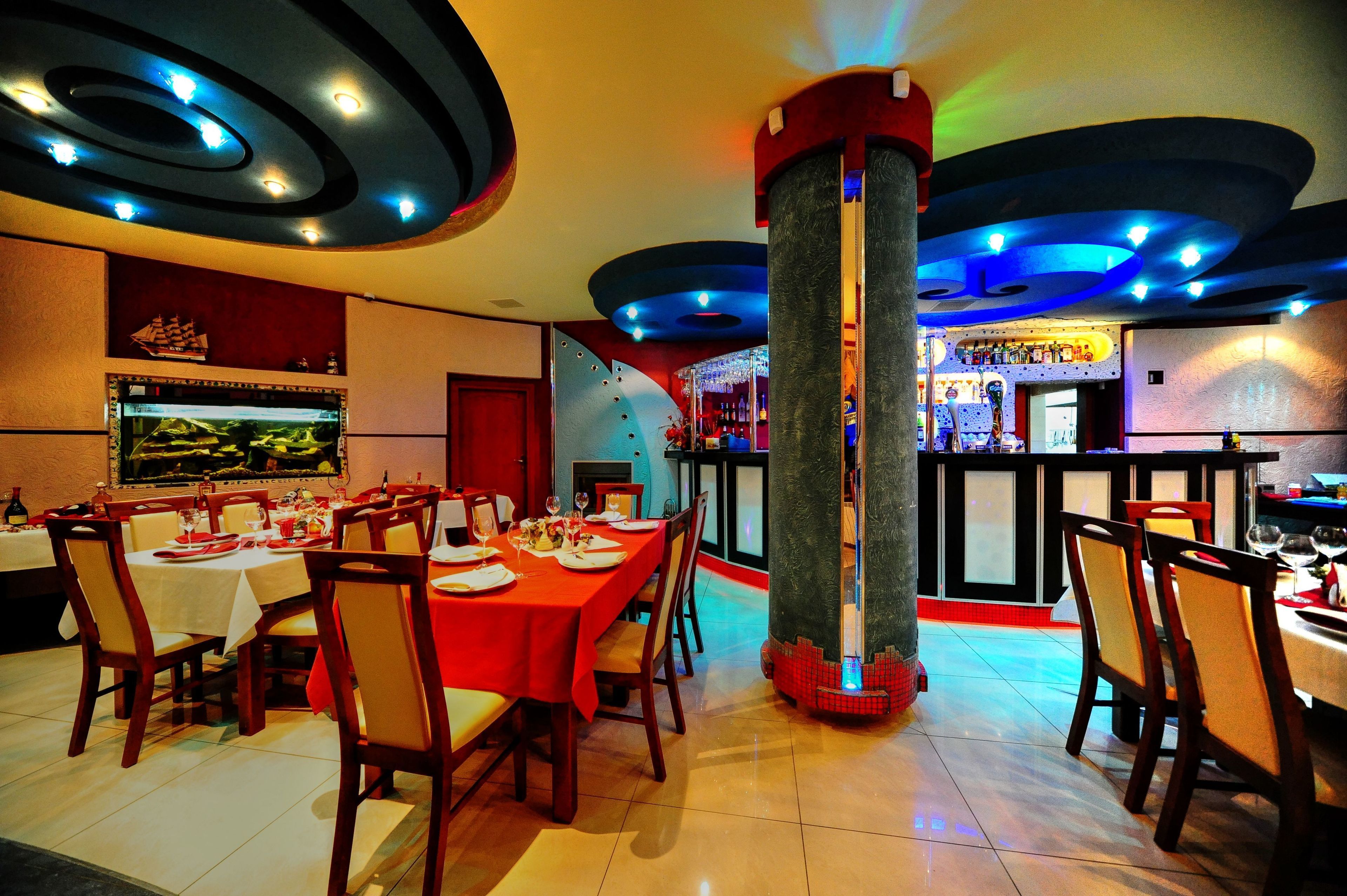 A restaurant with round tables, chairs, a bar area, and a large pillar.