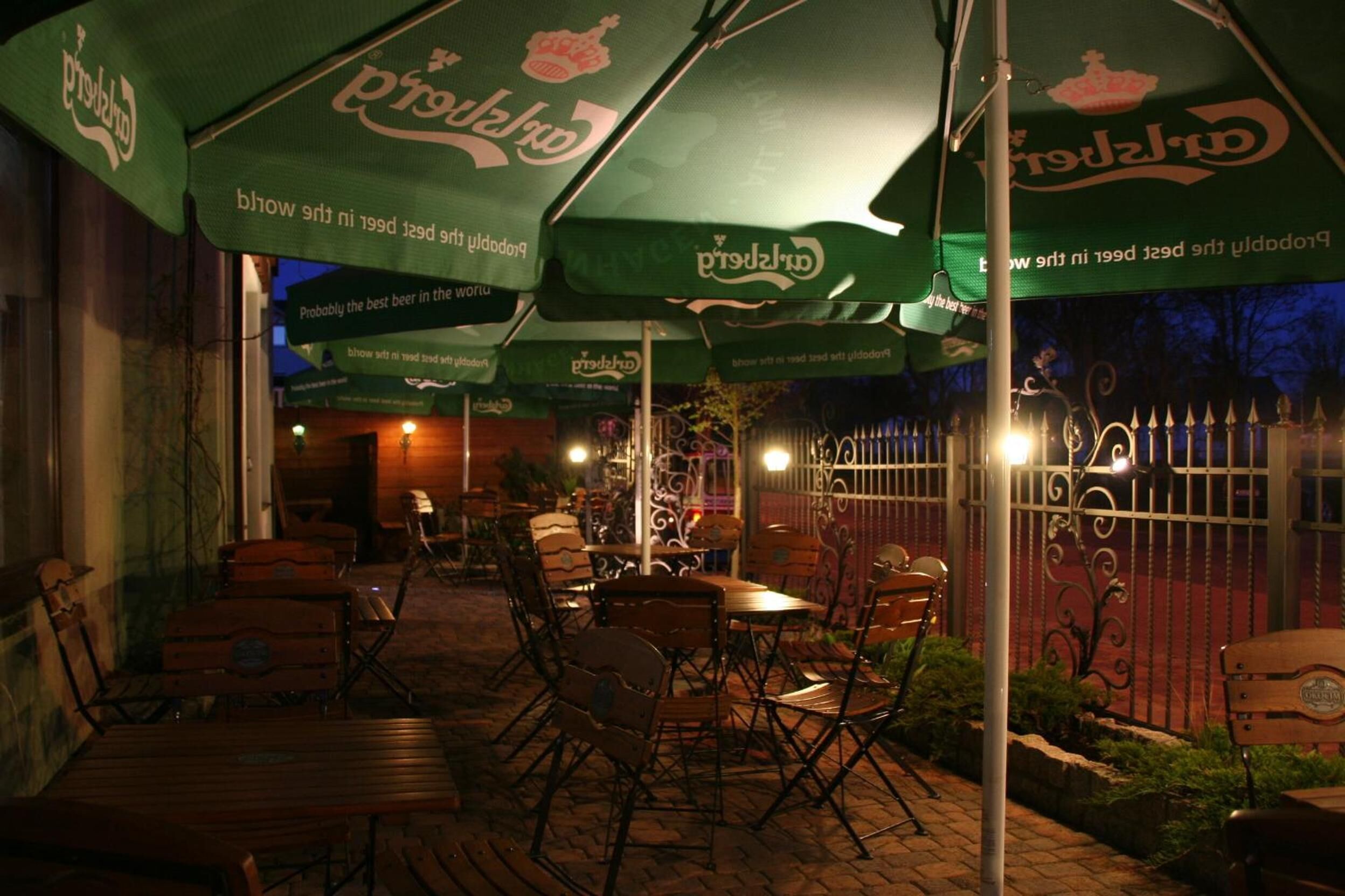 Area patio esterna con tavoli e sedie di legno, coperta da ombrelloni verdi con il logo "Petrus".