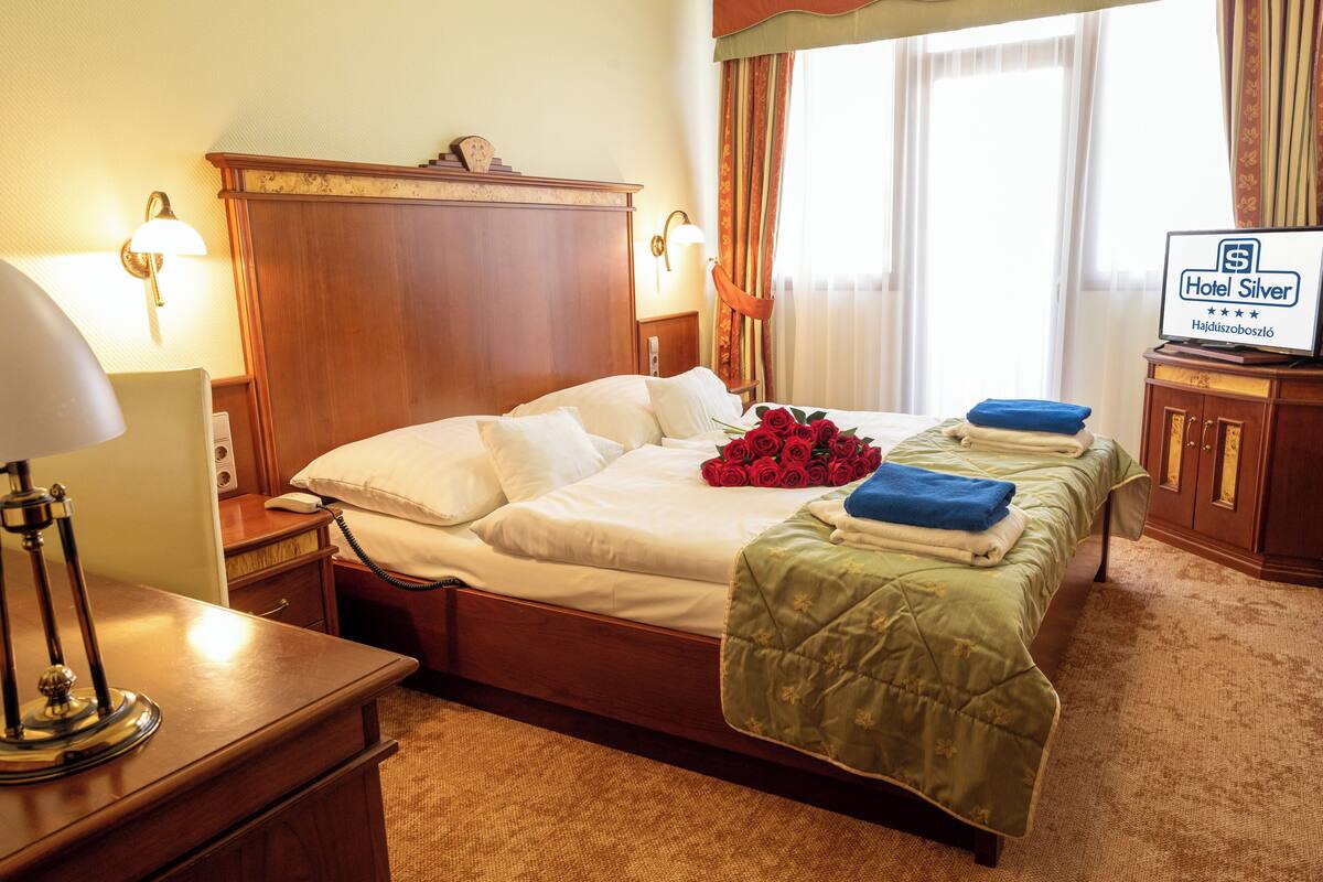Habitación de hotel con cama de madera, mesita de noche con lámpara, teléfono junto a la cama, colcha verde y un cartel que indica el nombre y la categoría del hotel.