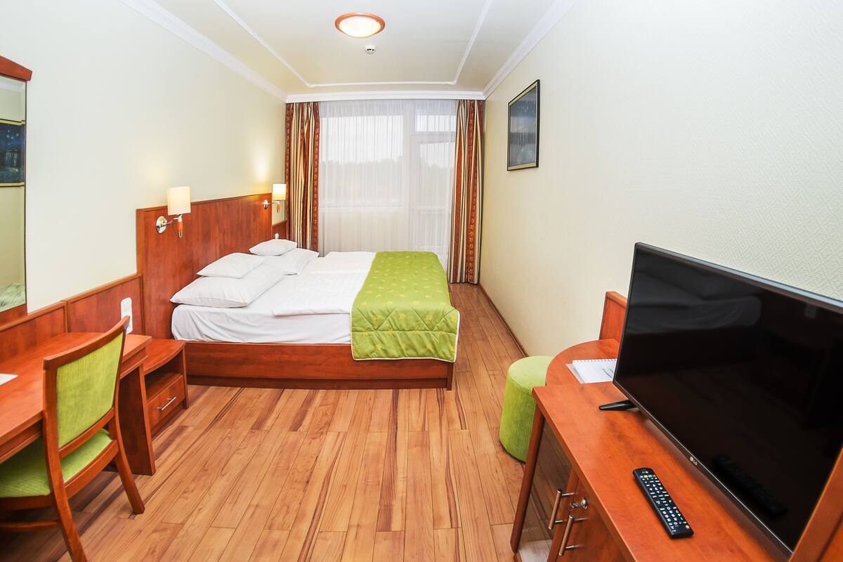 Una habitación de hotel con una cama de madera, un escritorio con silla, un televisor y una ventana con cortinas.