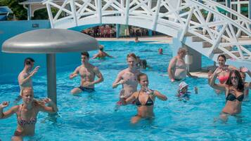 Una piscina con gente en el agua, una estructura de puente blanco y una zona de estar cubierta al fondo.