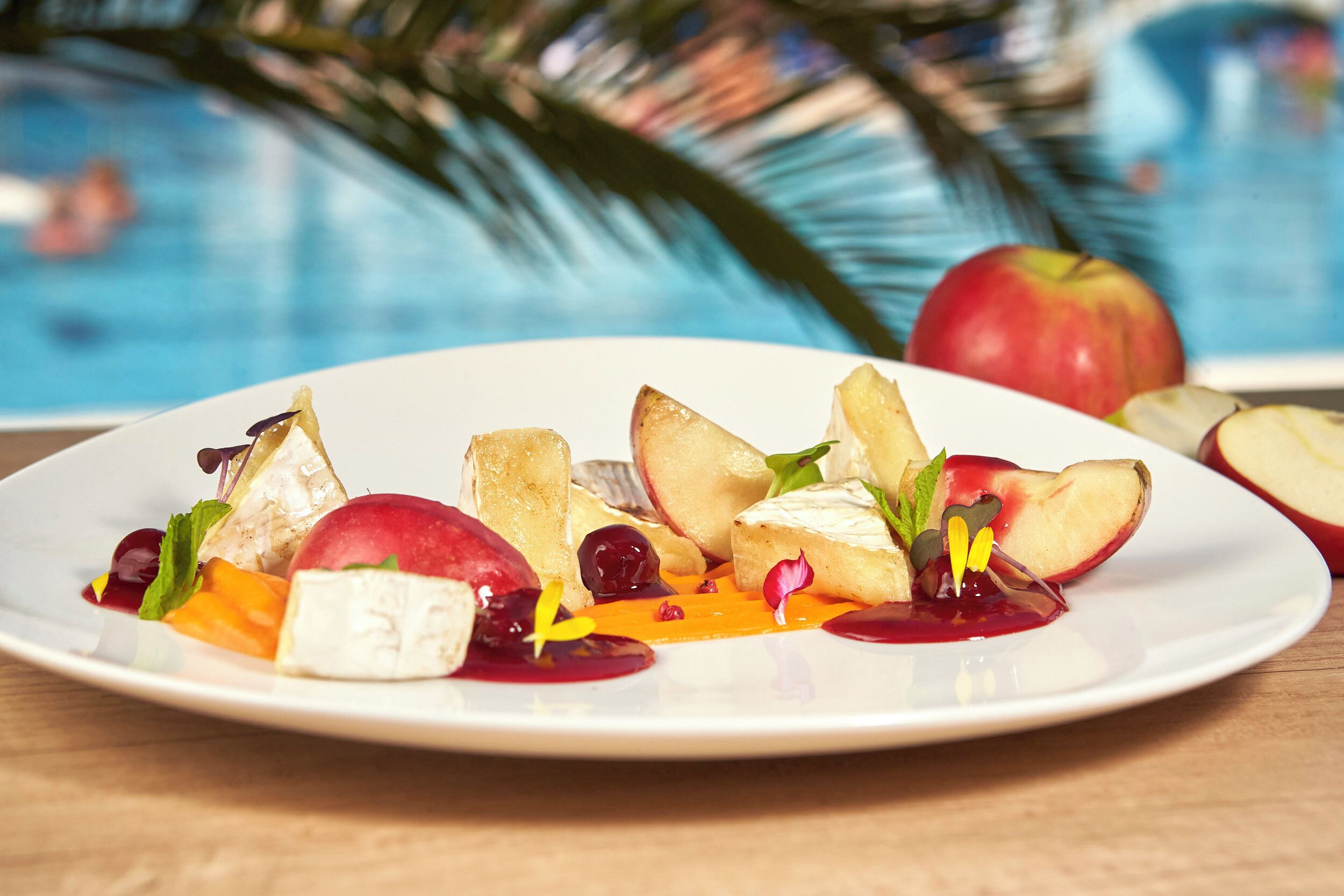 Ein Teller mit Essen, Früchten und Käse, im Hintergrund ein Pool und eine Palme.