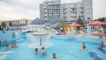 Area piscina con diversi livelli di elementi acquatici, un ponte e lettini.