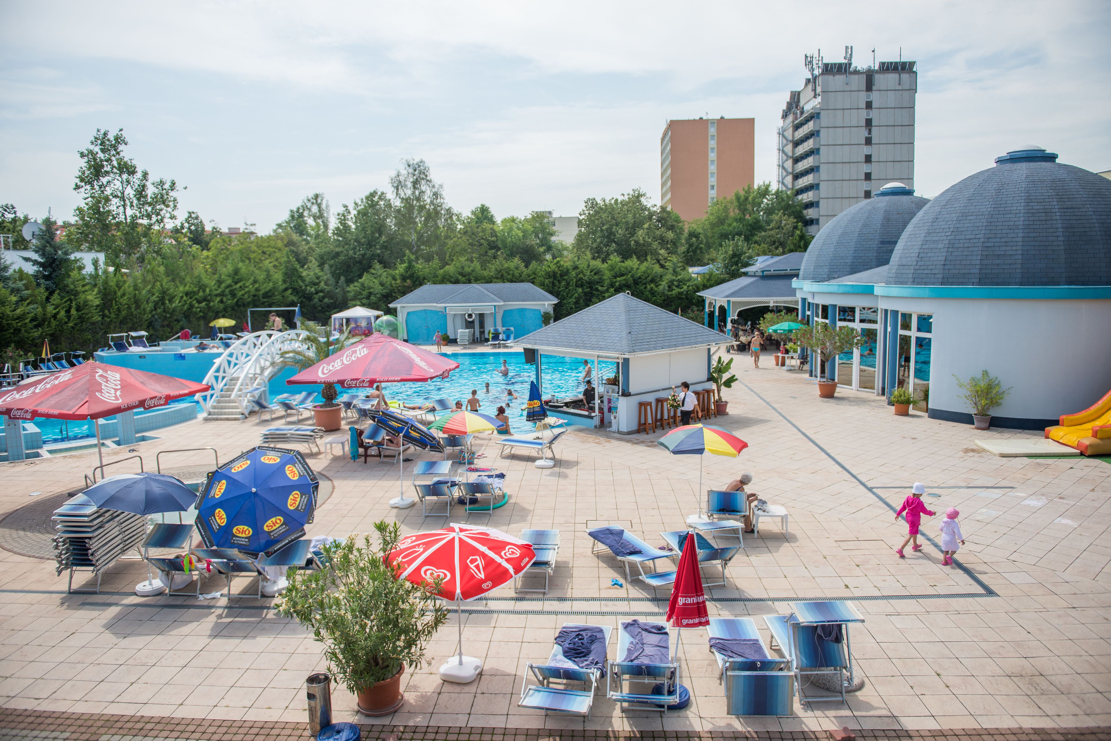 A pool area with lounge chairs, umbrellas, and a Coca-Cola branded water slide.