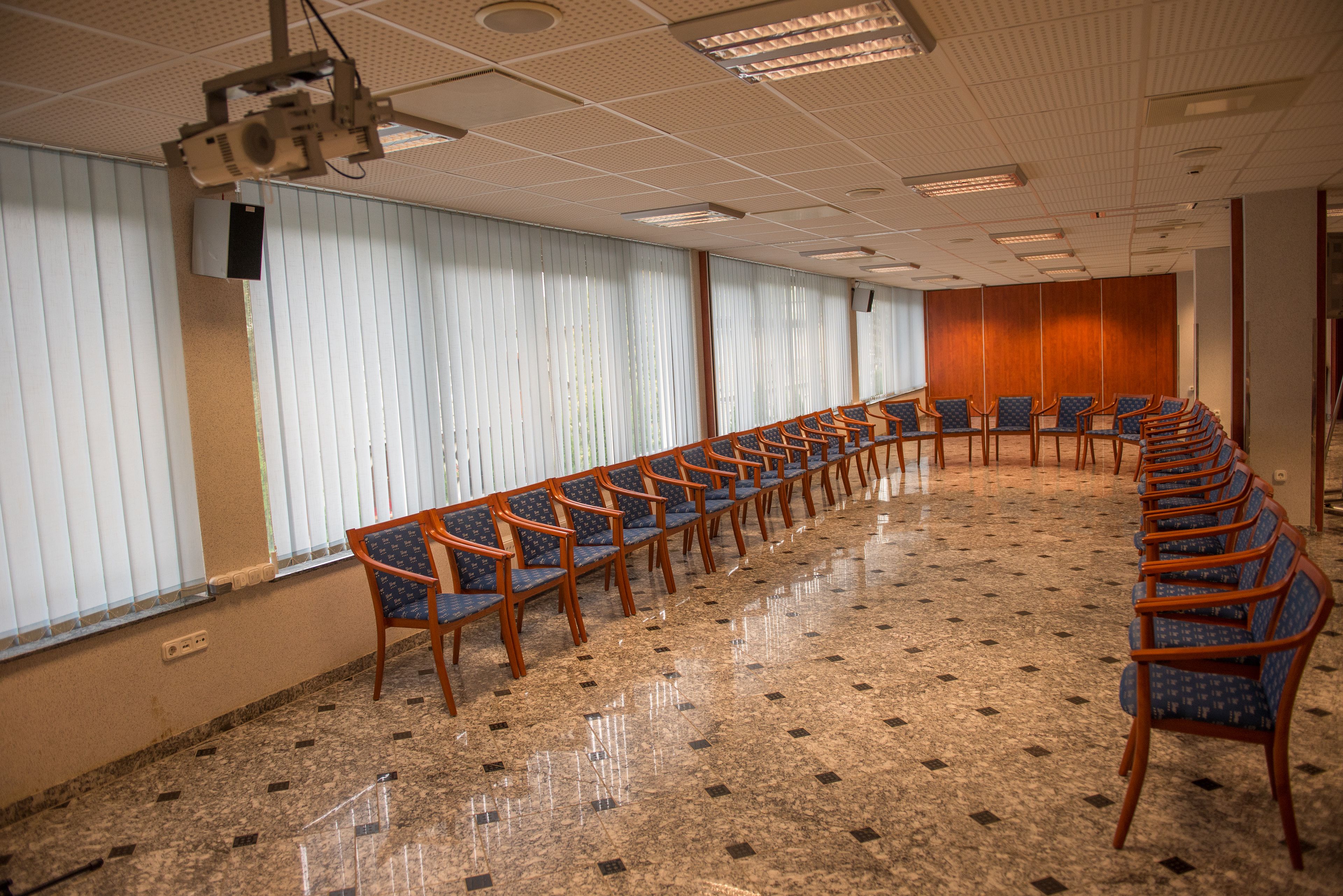 Ein Konferenzraum mit langem Tisch und Stühlen, großen Fenstern mit Jalousien und einer Decke mit eingelassenen Leuchten.