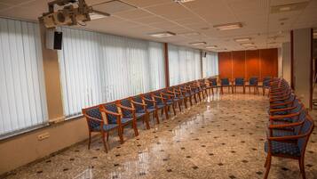Ein Konferenzraum mit langem Tisch und Stühlen, großen Fenstern mit Jalousien und einer Decke mit eingelassenen Leuchten.