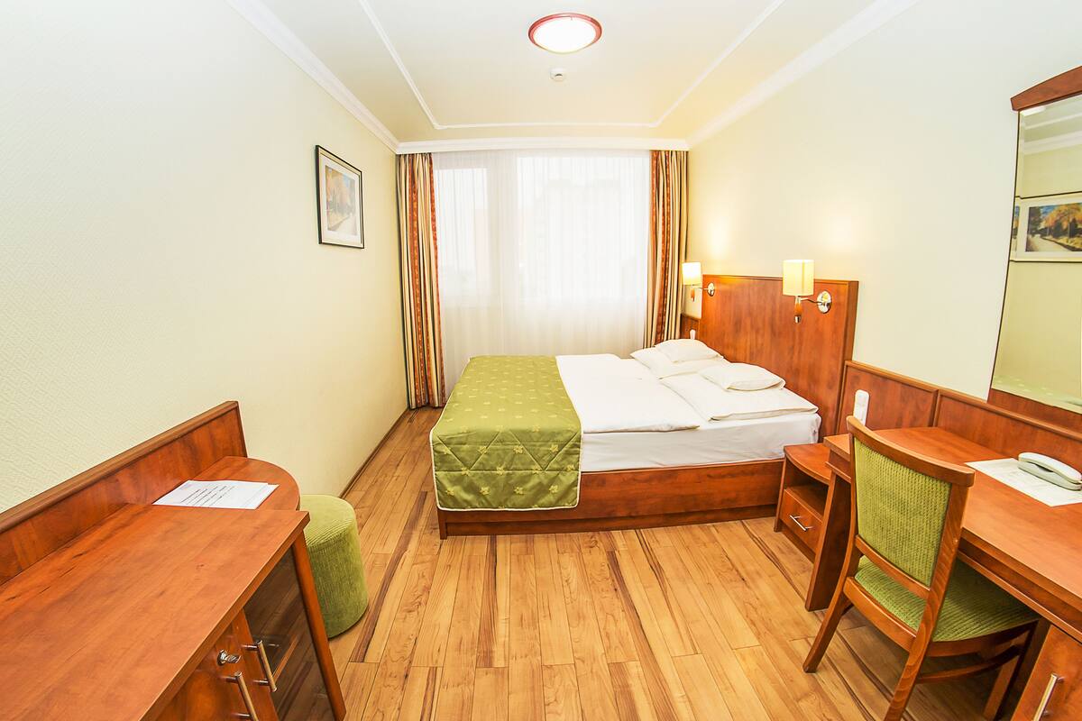 Una habitación de hotel con una cama de madera, un escritorio, una silla, un taburete pequeño y un espejo.