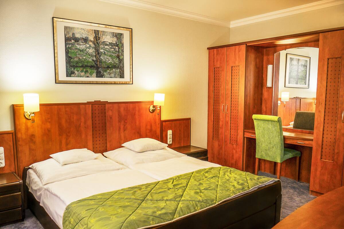 Habitación de hotel con una cama grande, un escritorio y una silla. Hay un cuadro en la pared y una lámpara en el escritorio.
