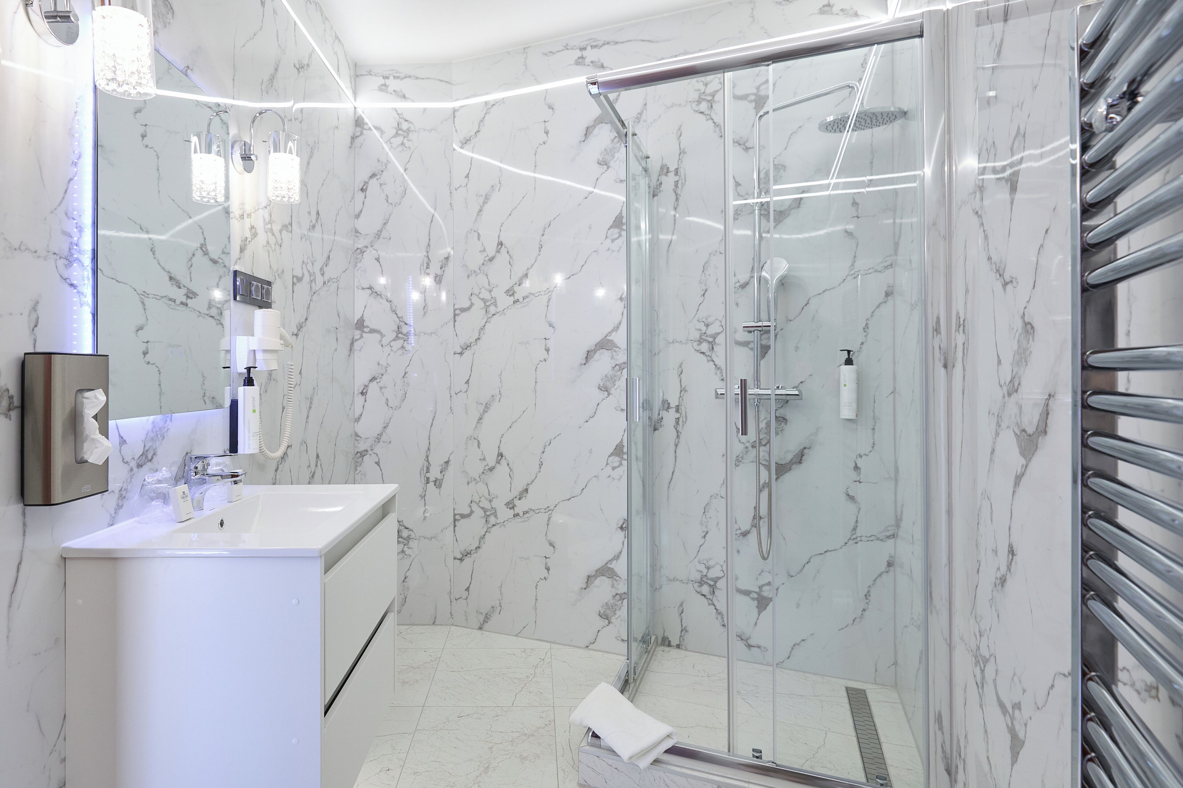 A modern bathroom with a glass-enclosed shower, a white sink, and marble walls.