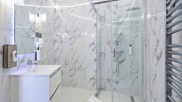 A modern bathroom with a glass-enclosed shower, a white sink, and marble walls.