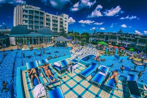 Zona de piscina con sillones de descanso, un tobogán y un edificio con varios balcones.