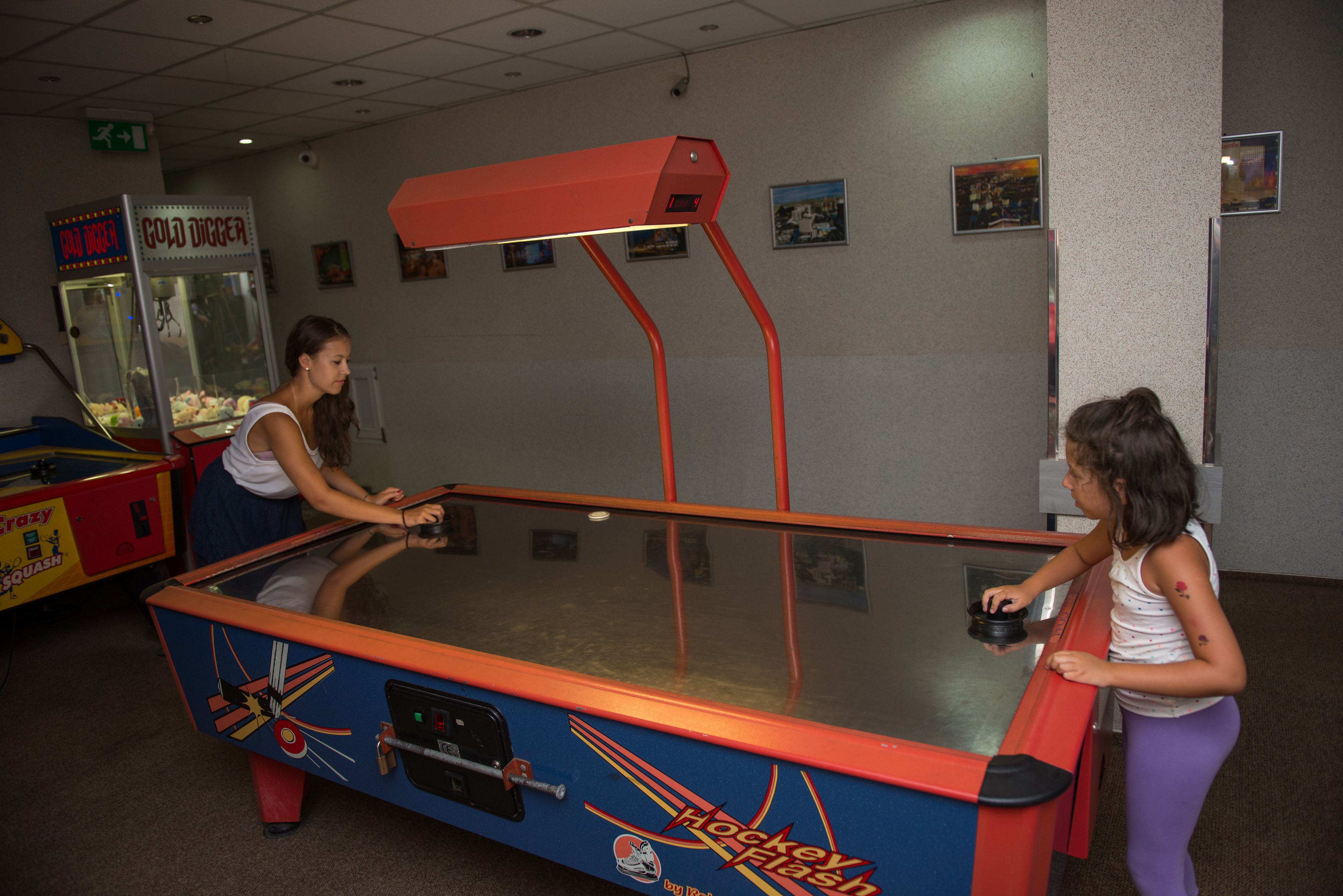Una mesa de hockey con superficie de vidrio y estructura roja, situada en una habitación con paredes decoradas con cuadros.
