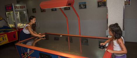 A table hockey game with a glass top and red frame, located in a room with walls decorated with framed pictures.