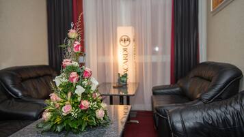 A room with a marble table, two leather chairs, a floral arrangement, and a sign with the word "CARDI" on a wall.