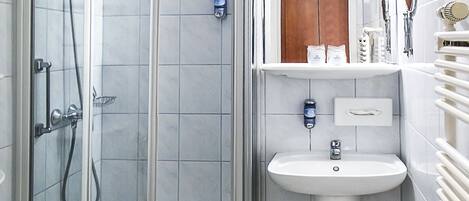 Un baño moderno con ducha de vidrio, lavamanos pedestal y tocador con espejo.