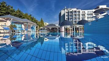 A swimming pool with clear blue water, surrounded by buildings with balconies and a covered area.
