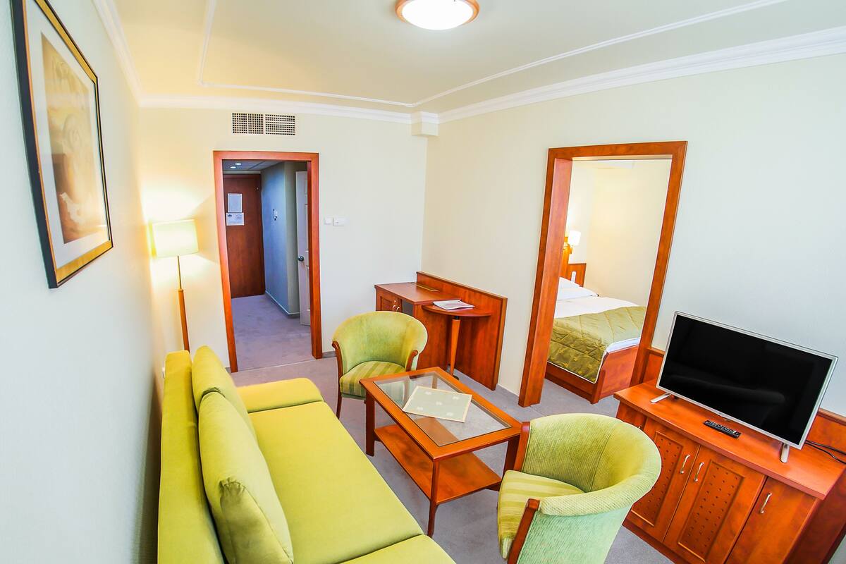 Una habitación de hotel con un sofá verde, una mesita, un televisor y un espejo.