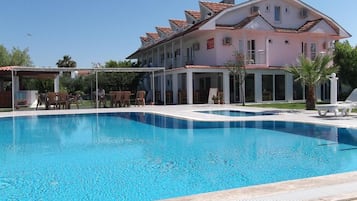 Piscina com espreguiçadeiras e um edifício com telhado cerâmico ao fundo.