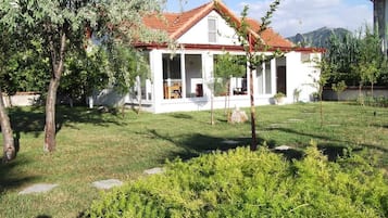 Una casa blanca con techo rojo, rodeada por un patio cubierto de césped y árboles.