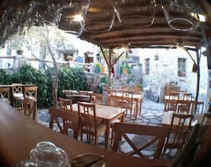 Un'area esterna con tavoli e sedie in legno, pareti in pietra e un'atmosfera rustica.