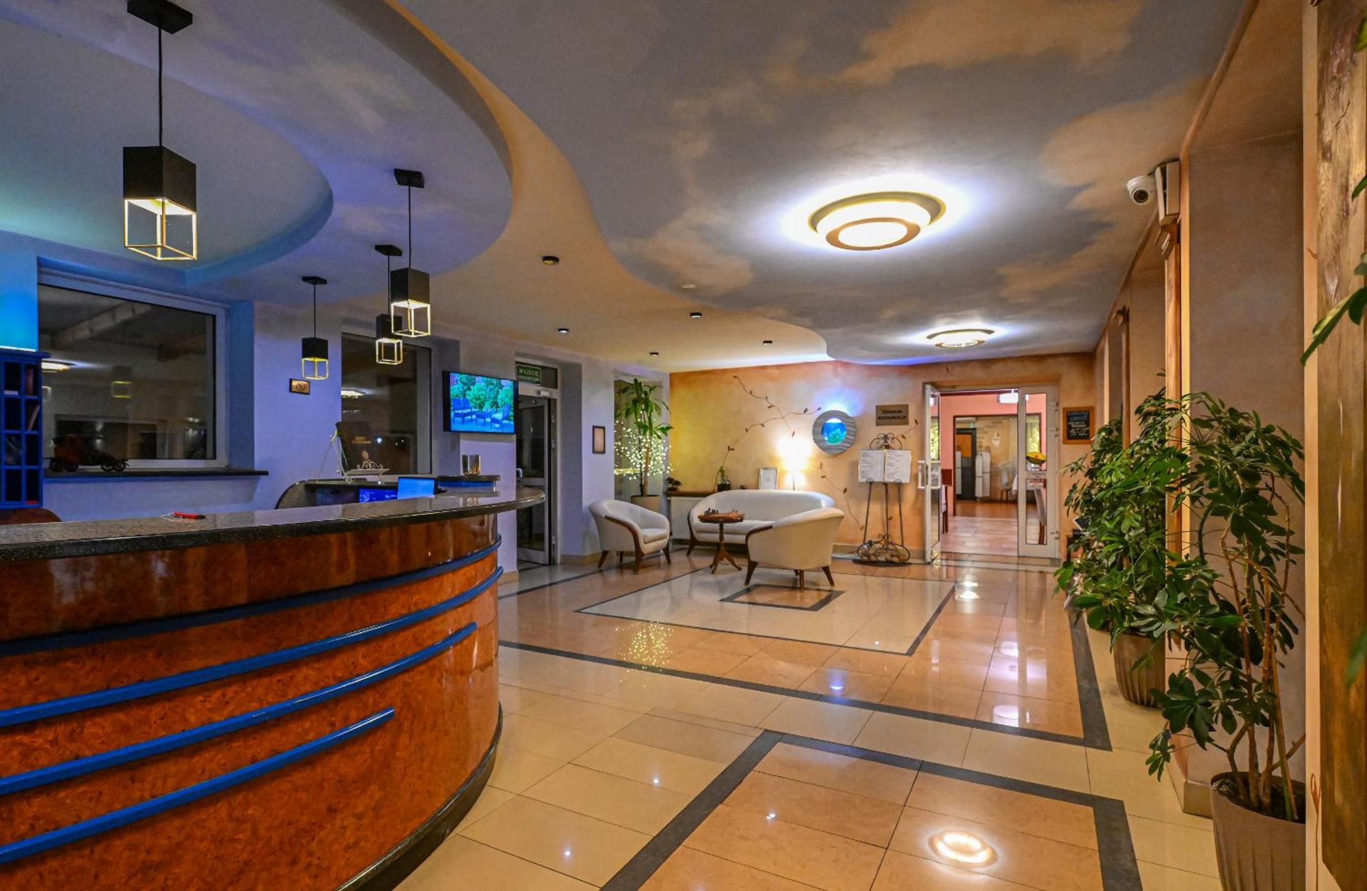 A hotel lobby with a reception desk, seating area, and a TV screen.