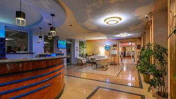 A hotel lobby with a reception desk, seating area, and a TV screen.